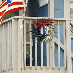 an american flag and wreath on the porch of a blue house with white railings