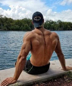 a shirtless man sitting on the edge of a dock looking out at some water