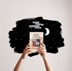 a person holding up a book in front of their face with black feathers on it