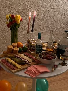 a table topped with lots of food next to bottles of wine and balloons in the air