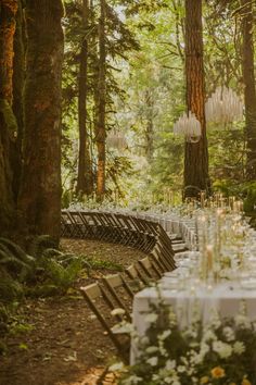 a long table set up in the woods for an outdoor wedding reception with chandeliers hanging from trees