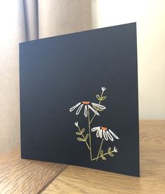 a black card with white and yellow flowers on the front, sitting on a wooden table