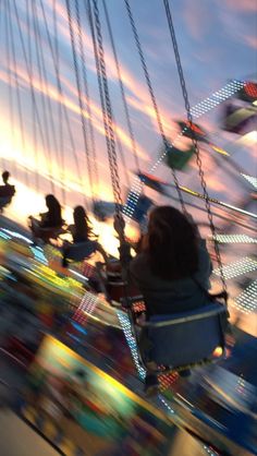 people ride on swings at an amusement park during the sunset or sunrise, with colorful lights in the background