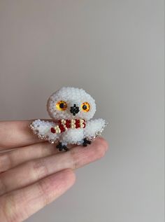 a hand holding a tiny white beaded owl