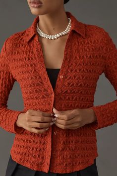 a woman in an orange cardigan with pearls on her neck and hands behind her back