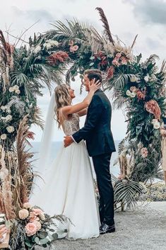 a bride and groom standing in front of an outdoor wedding arch with flowers on it