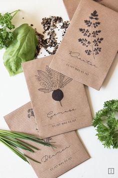 three napkins with designs on them sitting next to some herbs and other items that include lettuce