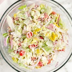 a glass bowl filled with salad on top of a white marble countertop next to a red and white towel