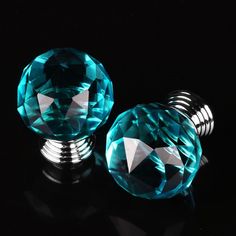 two blue glass knobs are on a black surface and one is in the shape of a ball