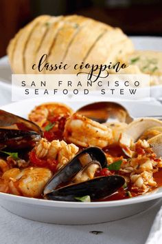 a white bowl filled with seafood and mussels on top of a table next to bread