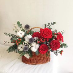 a basket filled with flowers and greenery on top of a white tablecloth covered bed