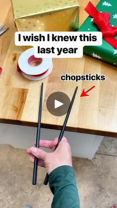 someone is holding two chopsticks in front of some wrapping paper on a table