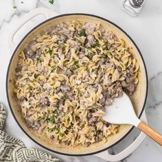 a skillet filled with pasta, meat and parsley on top of a marble counter