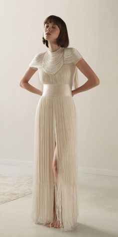 a woman wearing a long dress with fringes on the skirt and high heels standing in front of a white wall