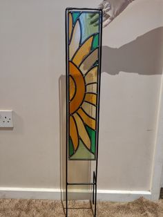 a stained glass sunflower on a stand in front of a white wall and tan carpet