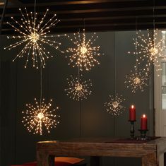 some lights are hanging from the ceiling above a dining room table with red chairs and candles