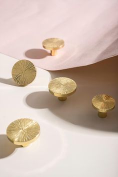 three golden knobs on the side of a white table with pink sheets in the background