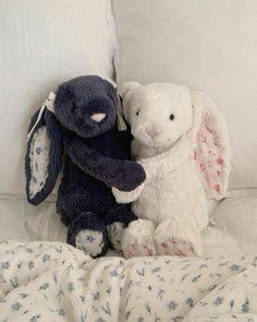 two stuffed animals sitting next to each other on a bed