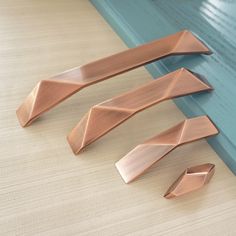 three pieces of copper metal sitting on top of a wooden floor next to a blue door