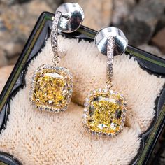 This wonderful pair of pierced earrings feature an 18K yellow gold dangle style halo setting and topped with a platinum half hoop. Each earring is accented with one (1) cushion modified brilliant cut fancy yellow colored diamond surrounded by a halo of twenty-six (26) round diamonds all prong set. The top of each earring has a half hoop containing thirteen (13) diamonds set outside and inside of the hoop and all bead set. The earrings are finished with a post and la pousette backs. The earring measure 22.7mm from top to bottom of dangle and have a width of 9.51mm. Luxury Yellow Diamond Drop Earrings, Luxury Diamond Earrings With Halo Design, Luxury Yellow Gold Earrings With Halo Design, Luxury Diamond Earrings With Halo Design For Evening, Luxury Halo Design Diamond Earrings For Evening, Yellow Halo Design Earrings In Fine Jewelry, Yellow Halo Design Fine Jewelry Earrings, Fine Jewelry Yellow Earrings With Halo Design, Yellow Halo Design Earrings Fine Jewelry