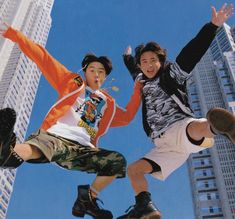 two young men jumping in the air on skateboards with buildings in the back ground