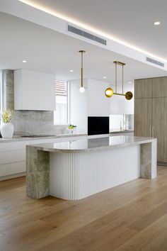 an empty kitchen with white cabinets and wood flooring is pictured in this image, there are lights hanging from the ceiling