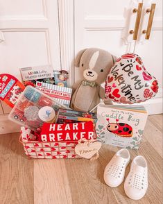 a teddy bear sitting on the floor next to a basket with books and other items