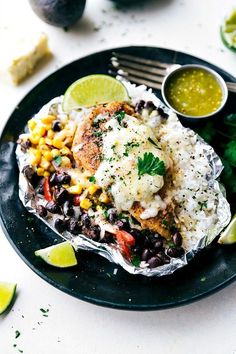 a black plate topped with chicken, rice and beans next to cilantro sauce