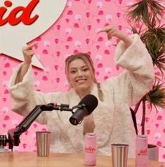 a woman is sitting at a table in front of a microphone and holding her hand up