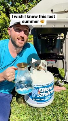 a man sitting in the grass next to an open propane tank with water on it