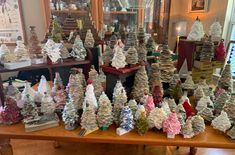 a table topped with lots of fake trees on top of a wooden table next to a window