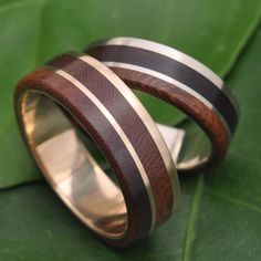 two wedding bands with wood and gold inlays on a green leafy background