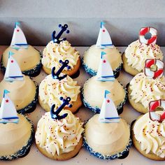 a box filled with cupcakes covered in frosting and topped with sailboats