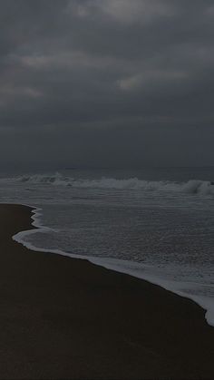 a person walking on the beach with an umbrella in their hand under a cloudy sky