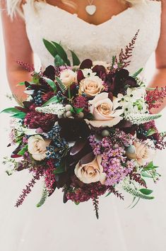 a bride holding a bouquet of flowers and greenery on her wedding day in front of the camera