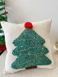 a crocheted christmas tree pillow sitting on top of a white couch next to a christmas tree