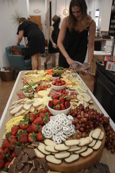 a woman standing in front of a table filled with fruits and cheeses on it