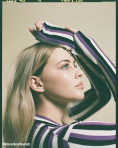 a woman with long blonde hair is wearing striped shirt and has her hands on her head