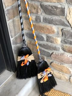 two black brooms with orange and white bows on them sitting next to a brick wall