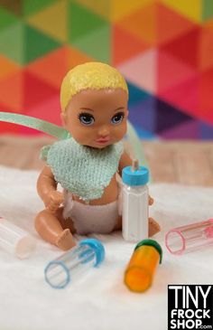 a small doll sitting on top of a table next to bottles and scissors with a ribbon around her neck