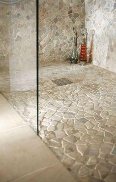 a bathroom with a glass shower door next to a tiled floor and walls, along with an orange vase on the corner