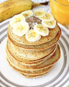 a stack of pancakes with banana slices on top and a glass of orange juice in the background