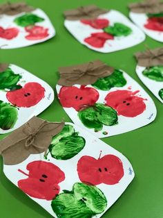 paper plates with apples painted on them and brown ribbon tied around the edges, sitting on a green surface