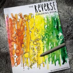 the reverse coloring book is next to a pencil and some watercolors on a furry surface