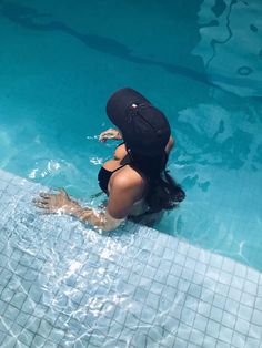 a woman in a black hat is sitting on the edge of a swimming pool