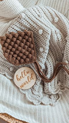 a knitted blanket with a wooden sign that says hello nature on it and two brown crocheted leaves