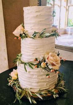 a three tiered white cake with flowers and greenery on the top is sitting on a table