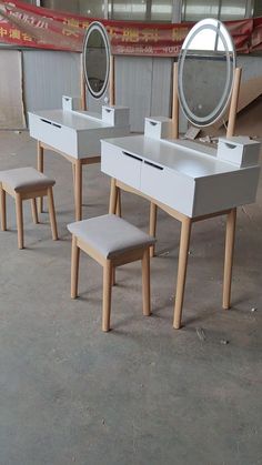 three vanity tables with stools and mirrors in an unfinished room, one is empty