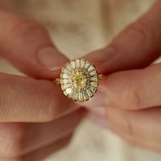 a woman's hand holding a ring with a yellow diamond in the middle,