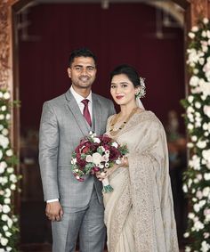 a man and woman standing next to each other in front of a doorway with flowers